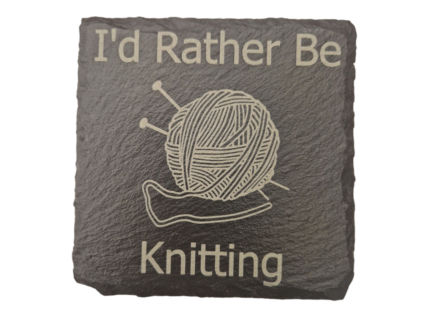 Square slate coaster with the text "I'd Rather Be" at the top of the coaster and "Knitting" at the bottom of the coaster. In the centre of the coaster is the image of a ball of wool with two knitting needles going diagonally through it.