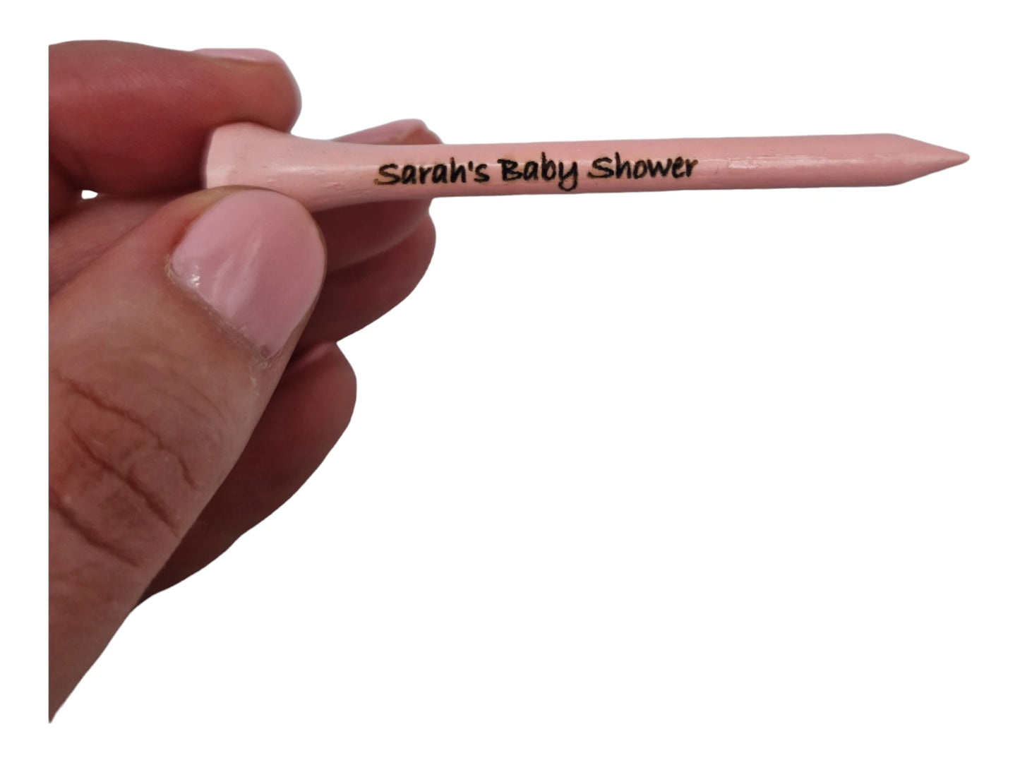 A hand holding a light pink 70mm golf tee with the text "Sarah's Baby Shower" laser engraved into it.