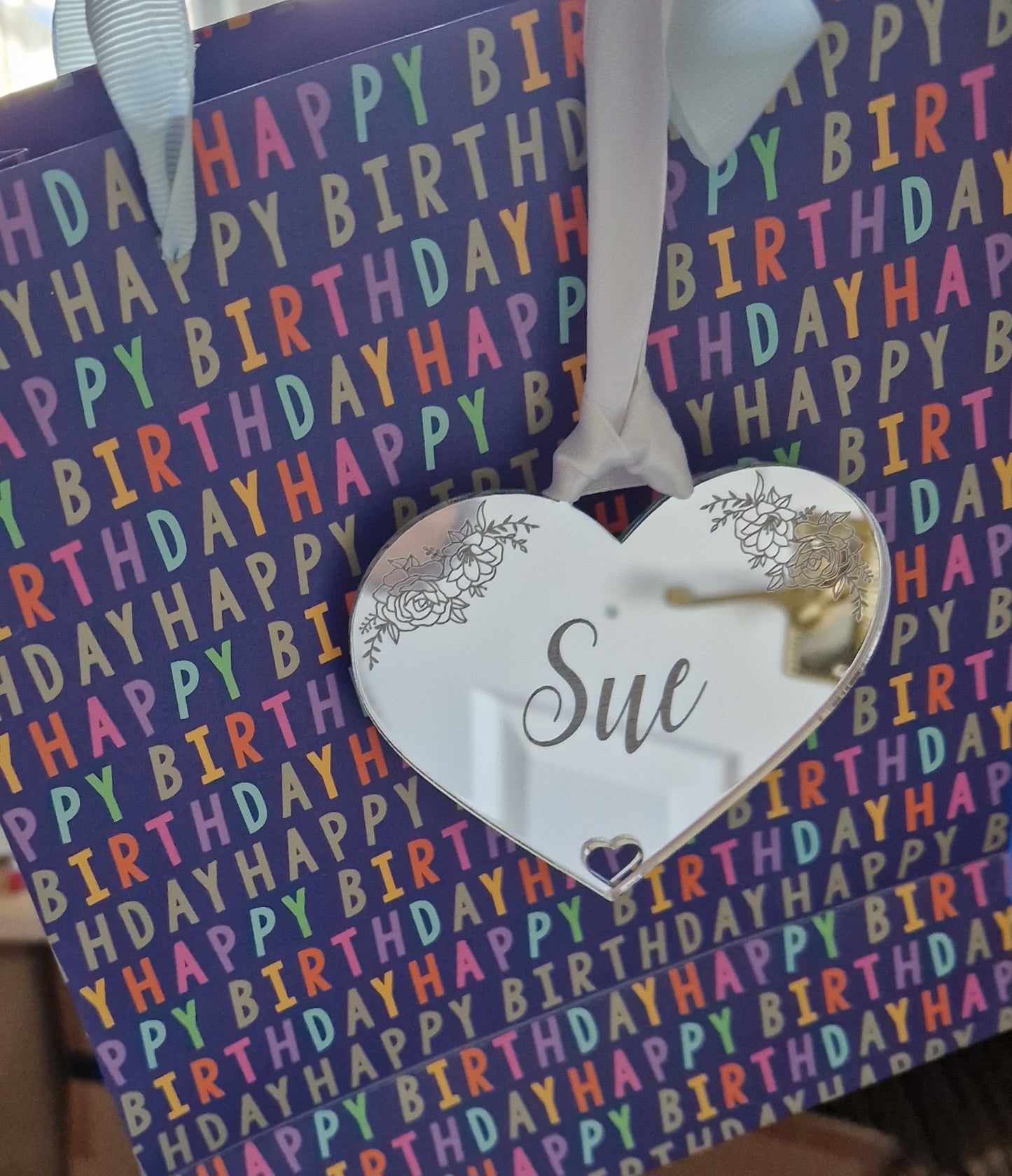 Silver acrylic heart shaped gift tag attached to a gift bag with white ribbon