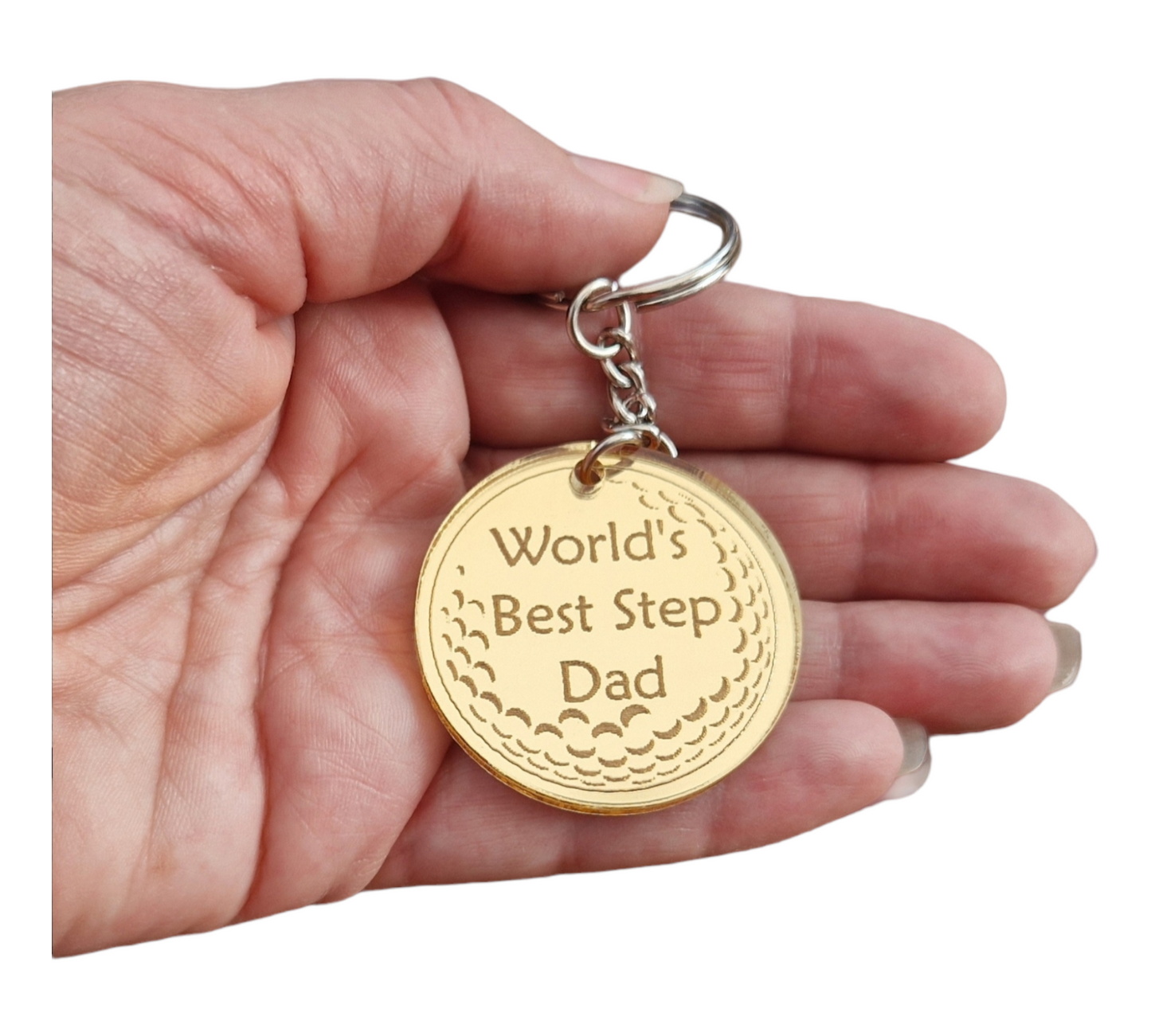 Gold mirror acrylic circle with the partial image of a golf ball with the text "World's Best Step Dad". Attached to the circle is a metal keychain. The keyring is being held.