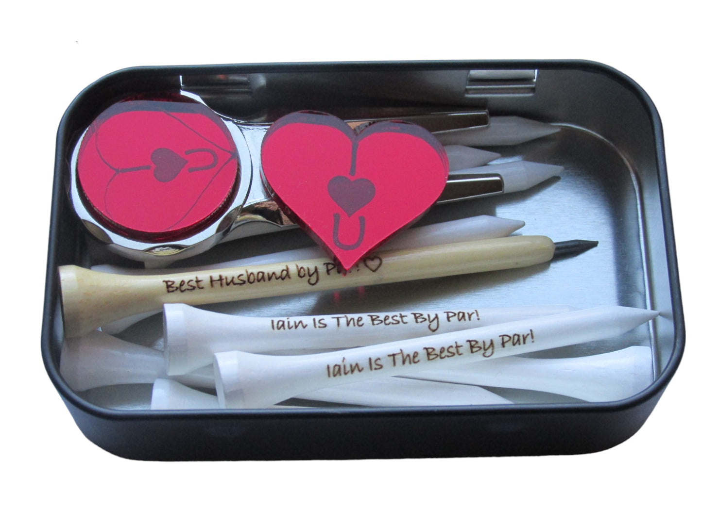 Natural pencil shaped like a golf tee with the text "Best Husband by Par!" and the outline of a heart engraved into it. 70mm tees with "Iain Is The Best By Par!" engraved into them, a metal pitch repairer with a red mirror acrylic circle at the top with "IU" and a heart engraved into the outline of a heart. A red heart shaped ball marker with "IU" and a heart engraved into it.These items are sitting inside a tin