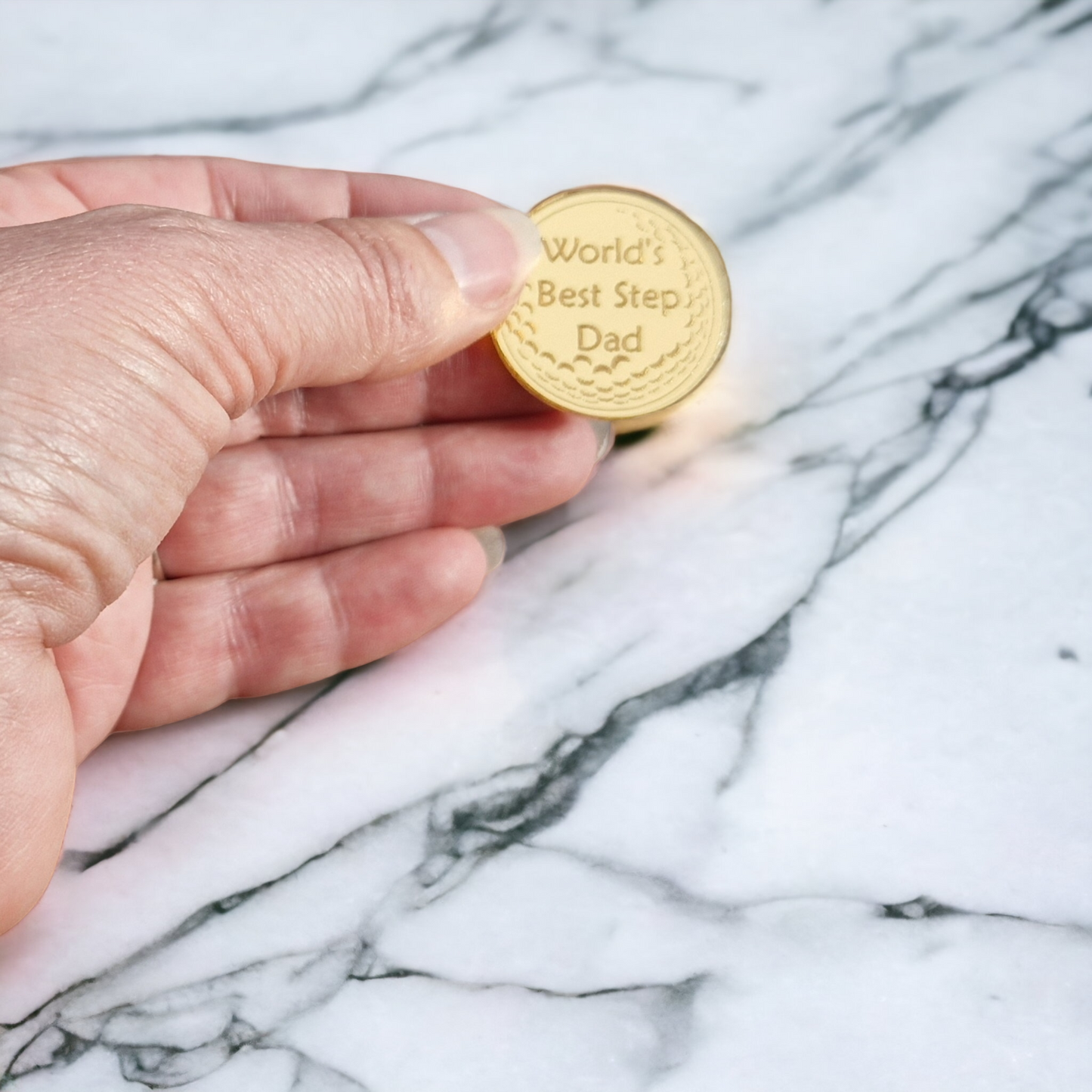 Gold ball marker with the partial image of a golf ball and the text "World's Best Step Dad" laser engraved into it