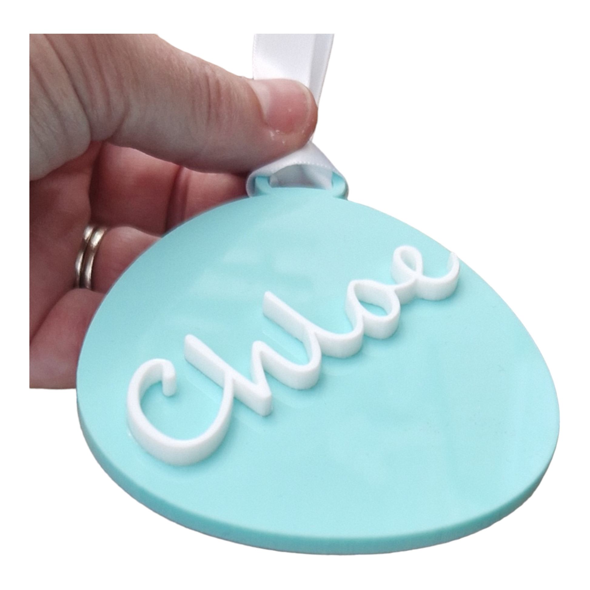 A hand holding an egg  shape in the colour Green Spearmint with the name Chloe in white going from the bottom to the top at at angle, with a ribbon for hanging. The Easter decoration is held at an angle to show that the name is 3D.