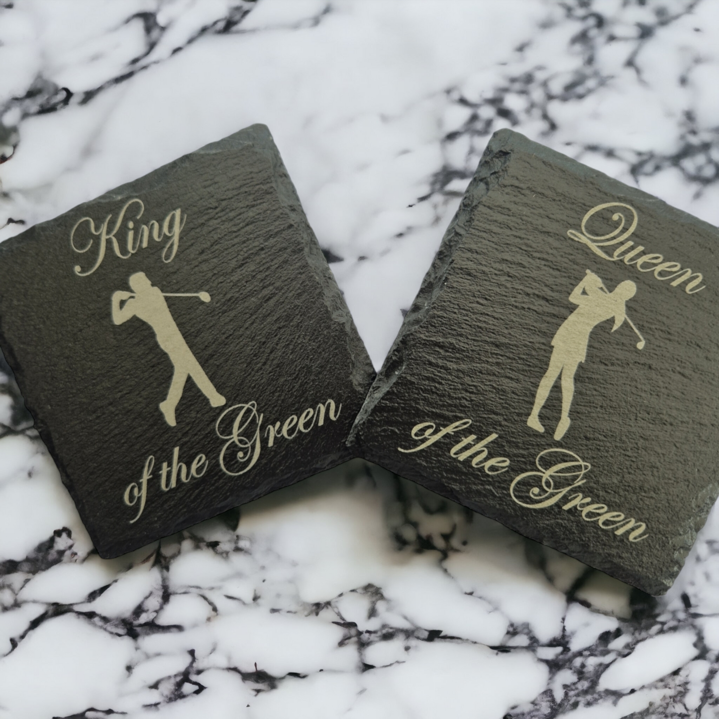 2 slate coasters - the lefthand coaster has the text "King of the Green" and the image of a male golfer. The righthand coaster has the text "Queen of the Green" and the image of a female golfer. The coasters are placed on a marble worktop 