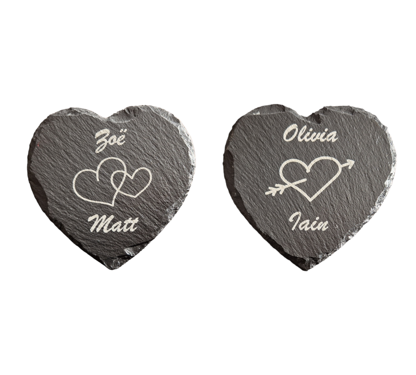 Two heart shaped slate coasters. The one on the left has "Zoe" engraved at the top of the coaster and "Matt" engraved at the bottom in cursive font. In the centre of the coaster there are two intertwined hearts. The coaster on the right has "Olivia" engraved at the top and "Iain" engraved at the bottom, with the image of a heart with an arrow running through it.